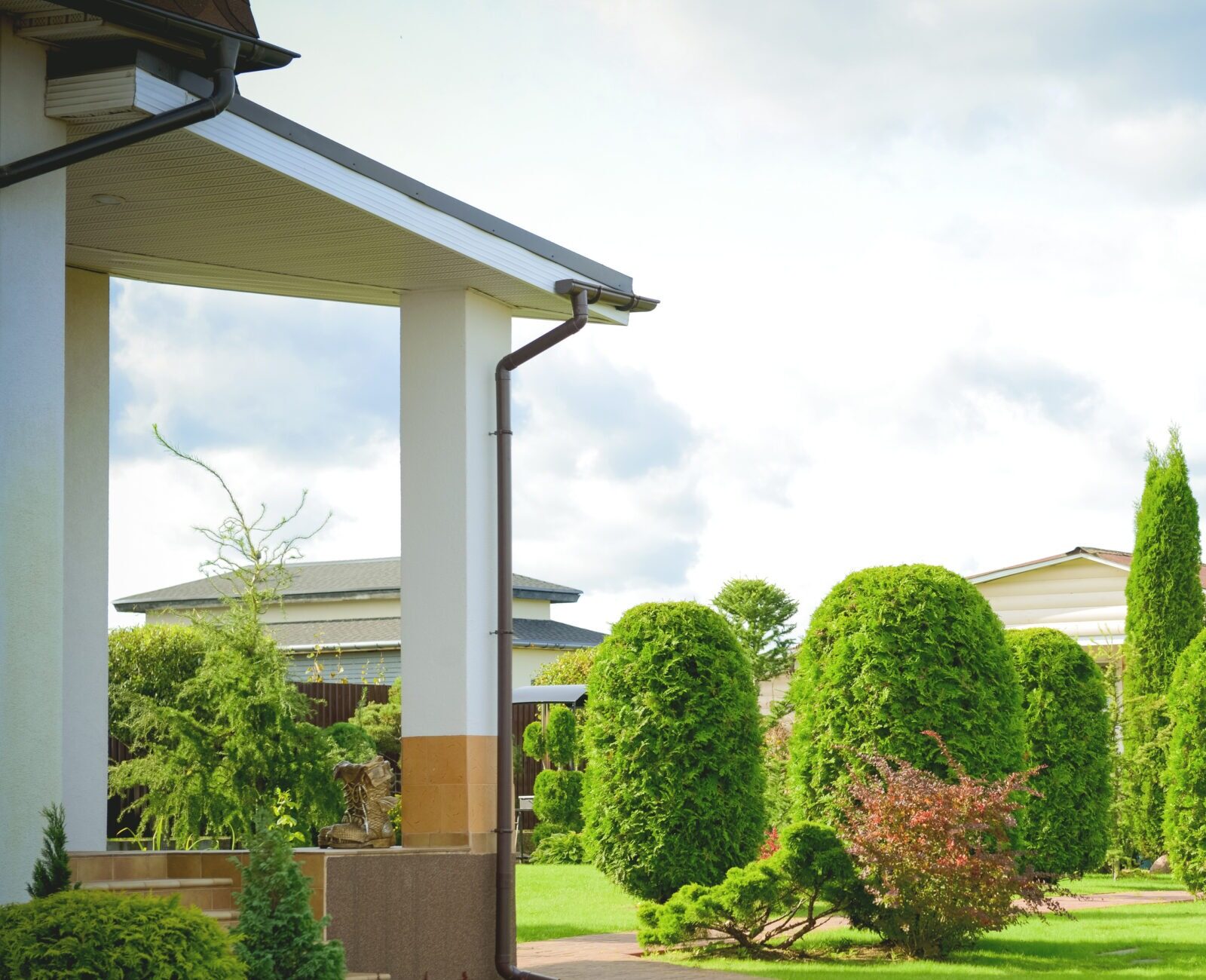 A well-manicured garden with neatly trimmed shrubs, surrounded by residential homes under a partly cloudy sky. No landmarks or people are visible.