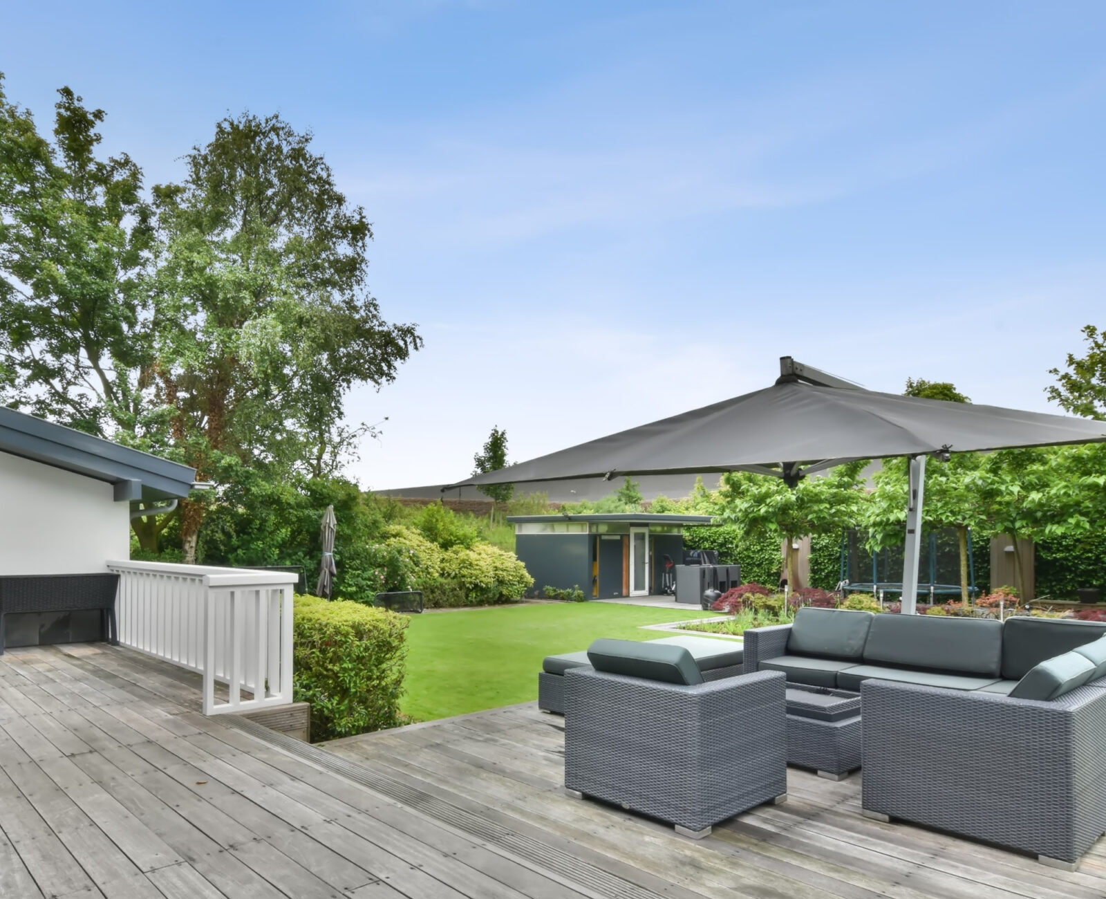 Spacious backyard features a wooden deck, modern outdoor furniture, large umbrella, and lush greenery, creating a serene and inviting atmosphere.