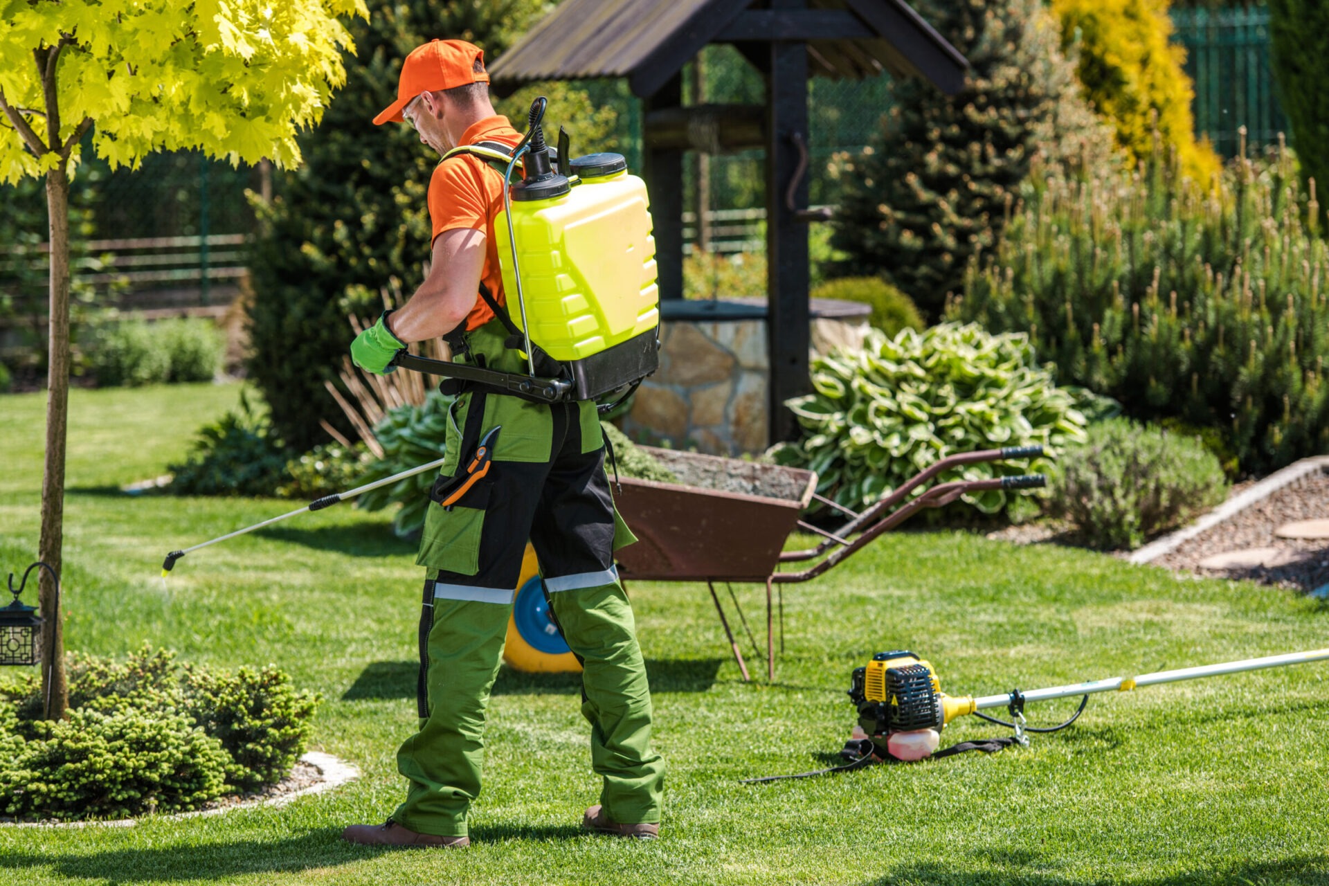 A person in orange and green clothing tends a garden with a yellow sprayer, surrounded by lush greenery and gardening tools.