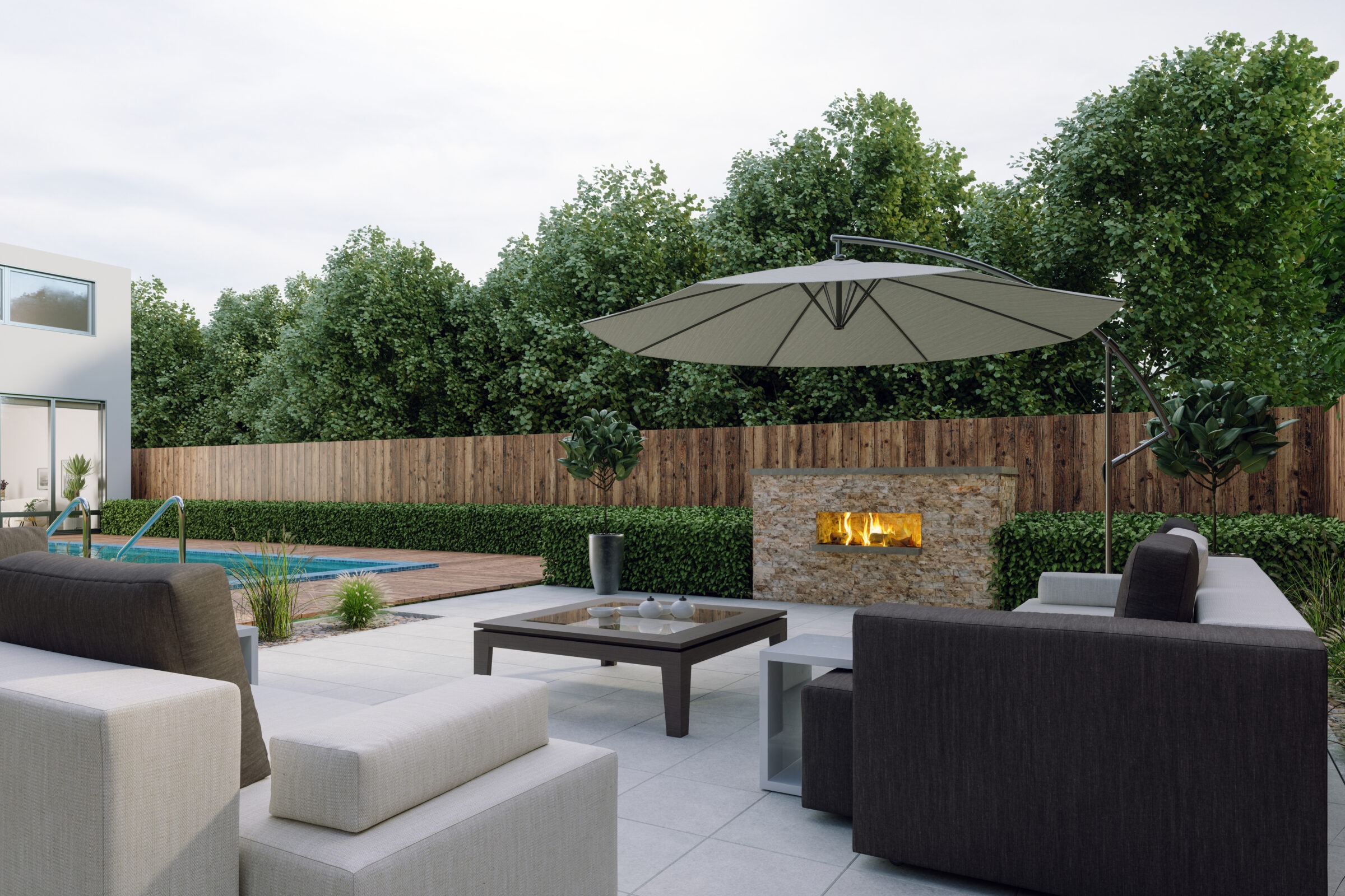 Modern patio features a cozy seating area, umbrella, and fire feature by a pool, surrounded by lush greenery and a wooden fence.