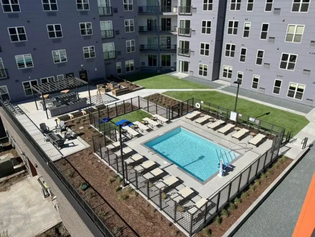 A commercial property with a pool surrounded by chairs and a metal fence in its courtyard.