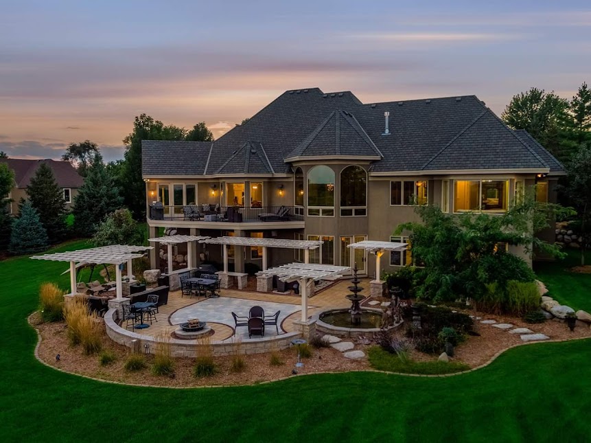 The backyard of a large home with a lush green lawn in the evening.