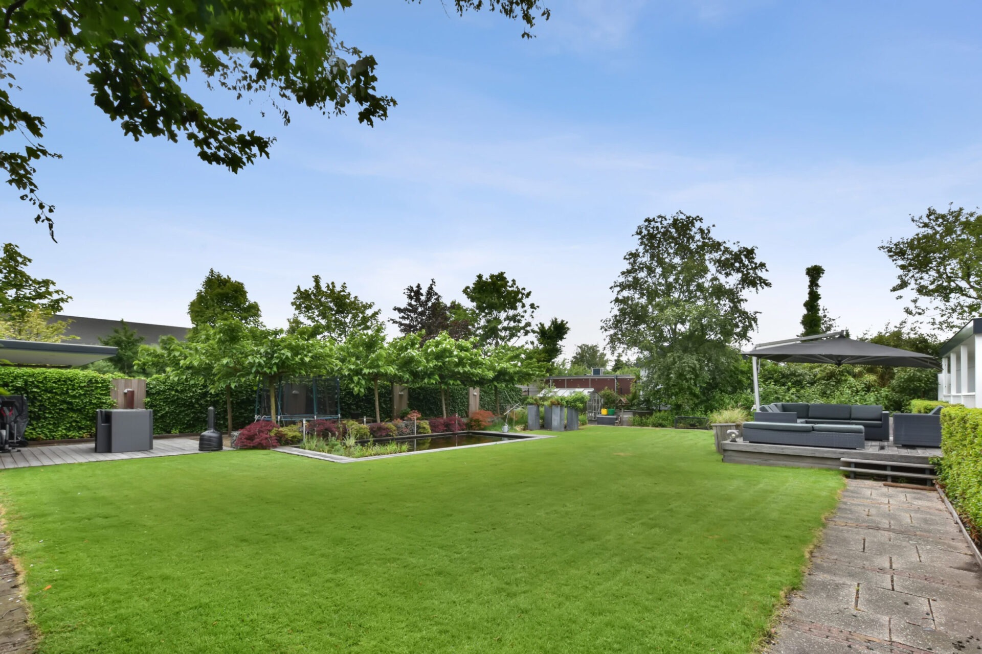 The backyard of the house with a large green lawn, a small swimming pool and a sitting area on a wooden floor