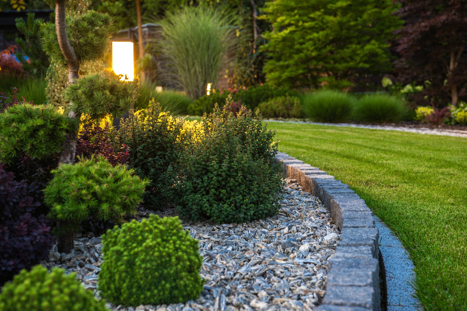 Masonry Edged Garden with Modern Illuminated by LED Light Posts and Decorative Plants in a Residential Backyard Garden.