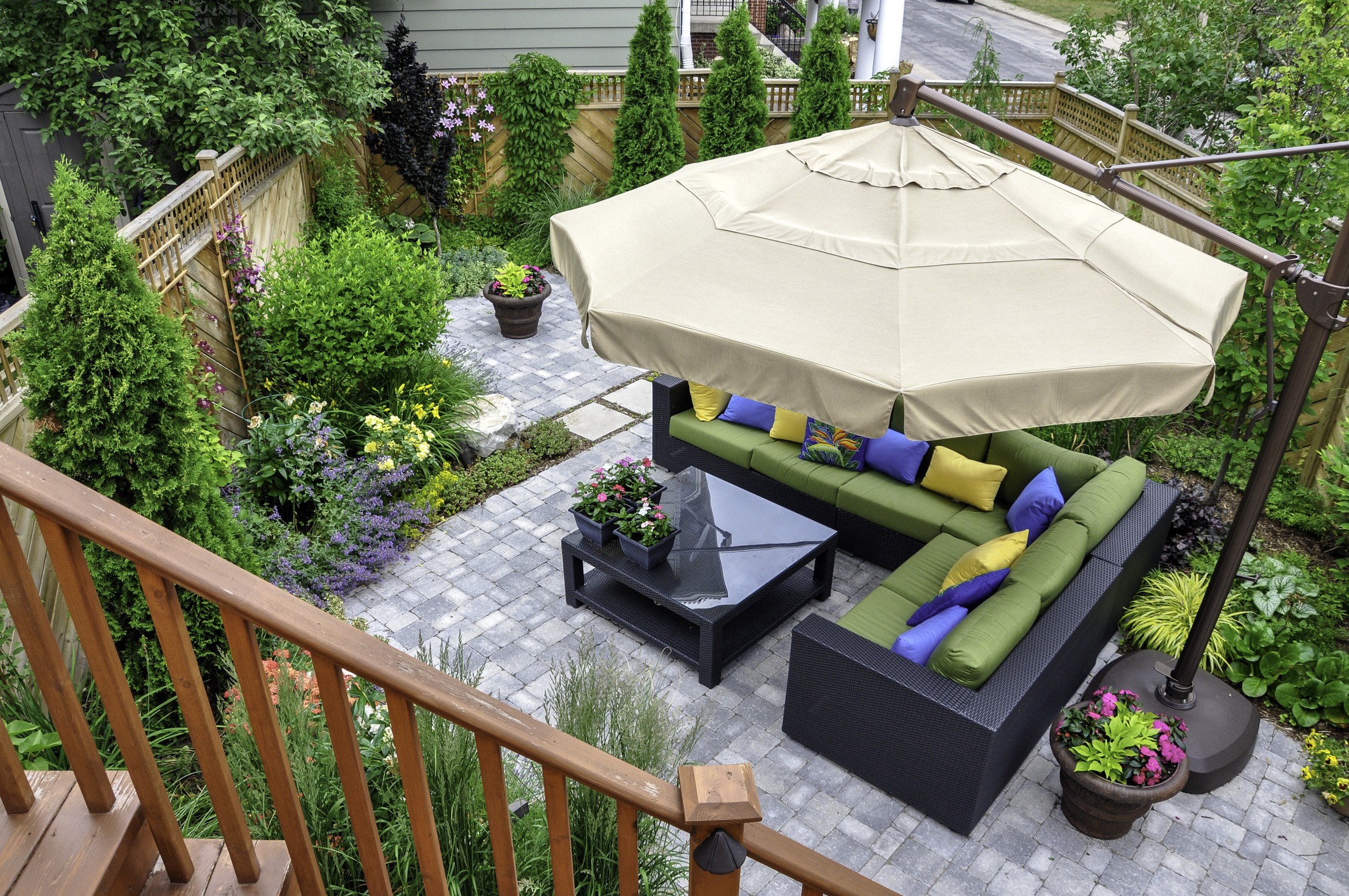 A beautiful small, urban backyard garden featuring a tumbled paver patio, flagstone stepping stones, and a variety of trees, shrubs and perennials add colour and year round interest.
