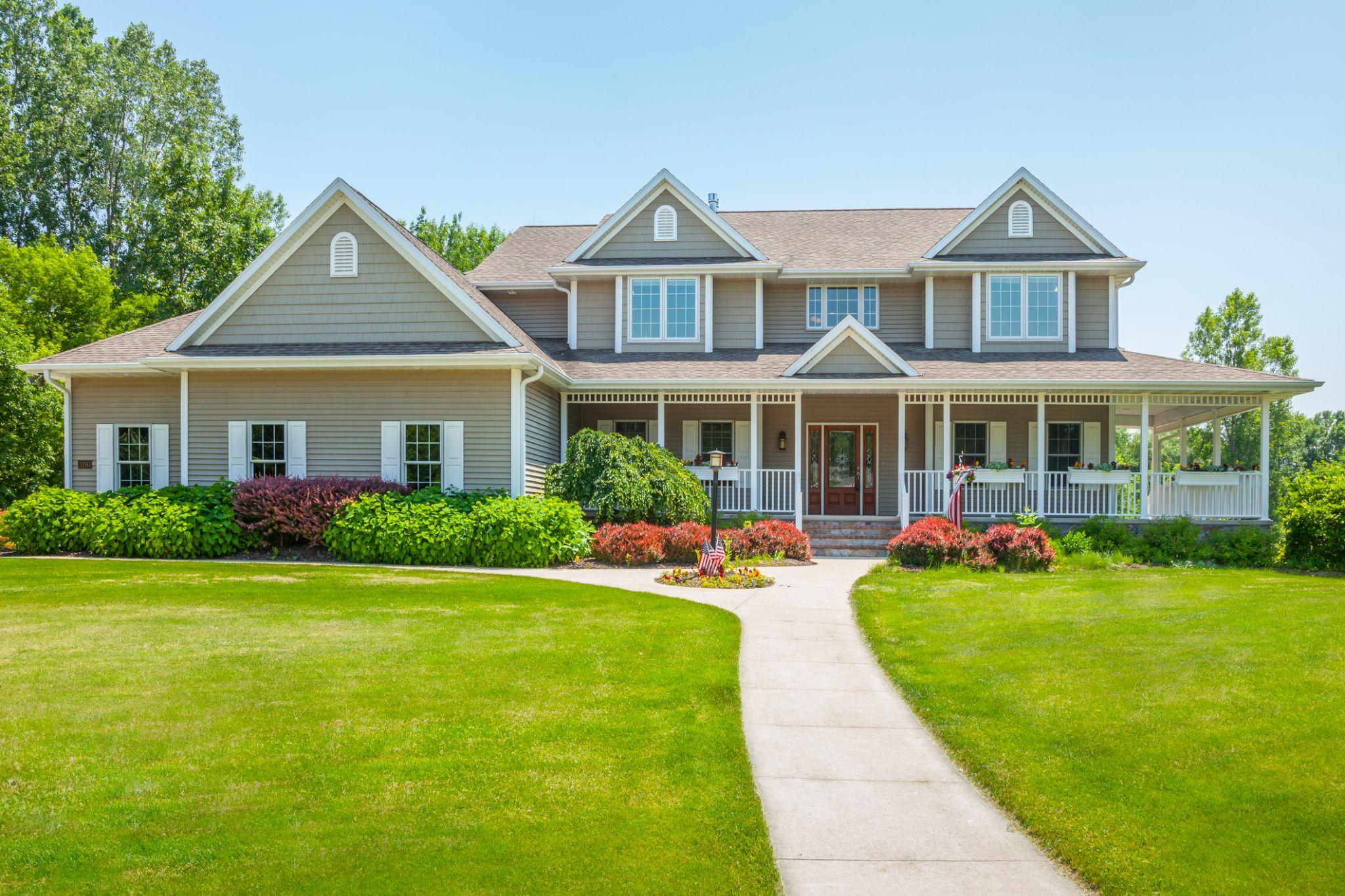 A house with wrap-around porch, curved walkway, and landscaped front yard