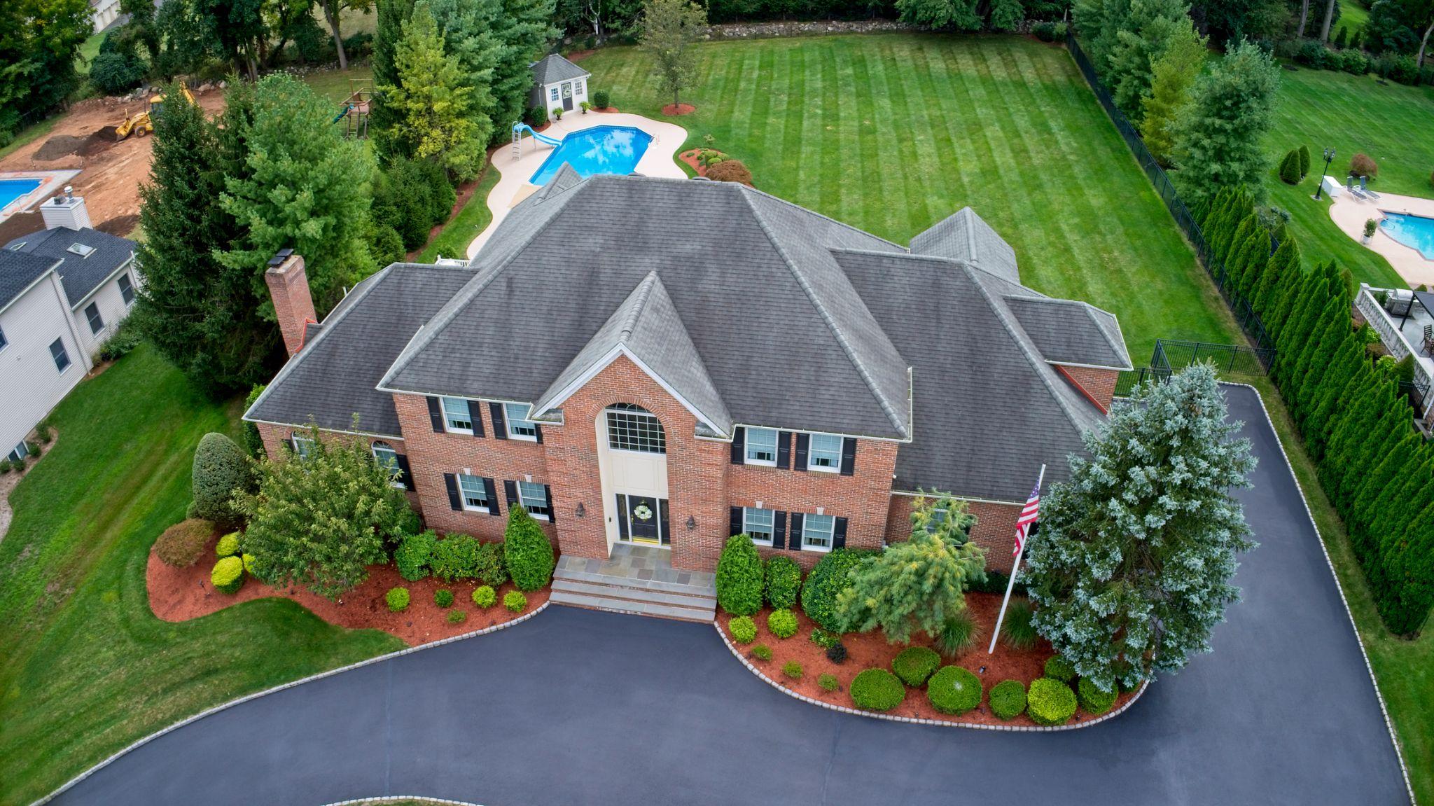 Aerial view of brick home with pool, striped lawn, and landscaped grounds