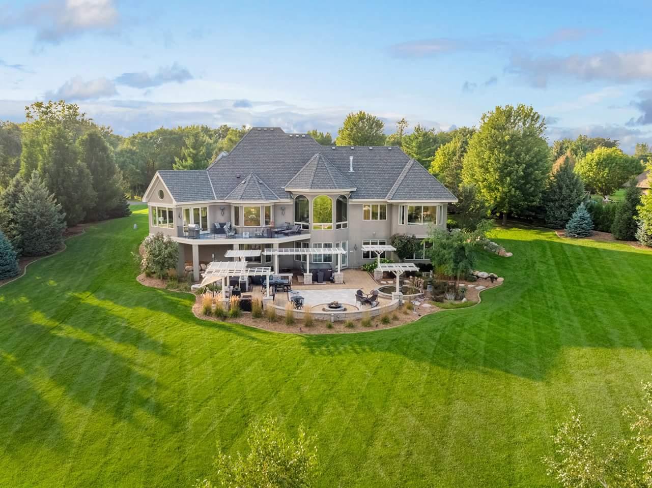 Aerial view of large home with patio, pergola, fire pit, and manicured lawn