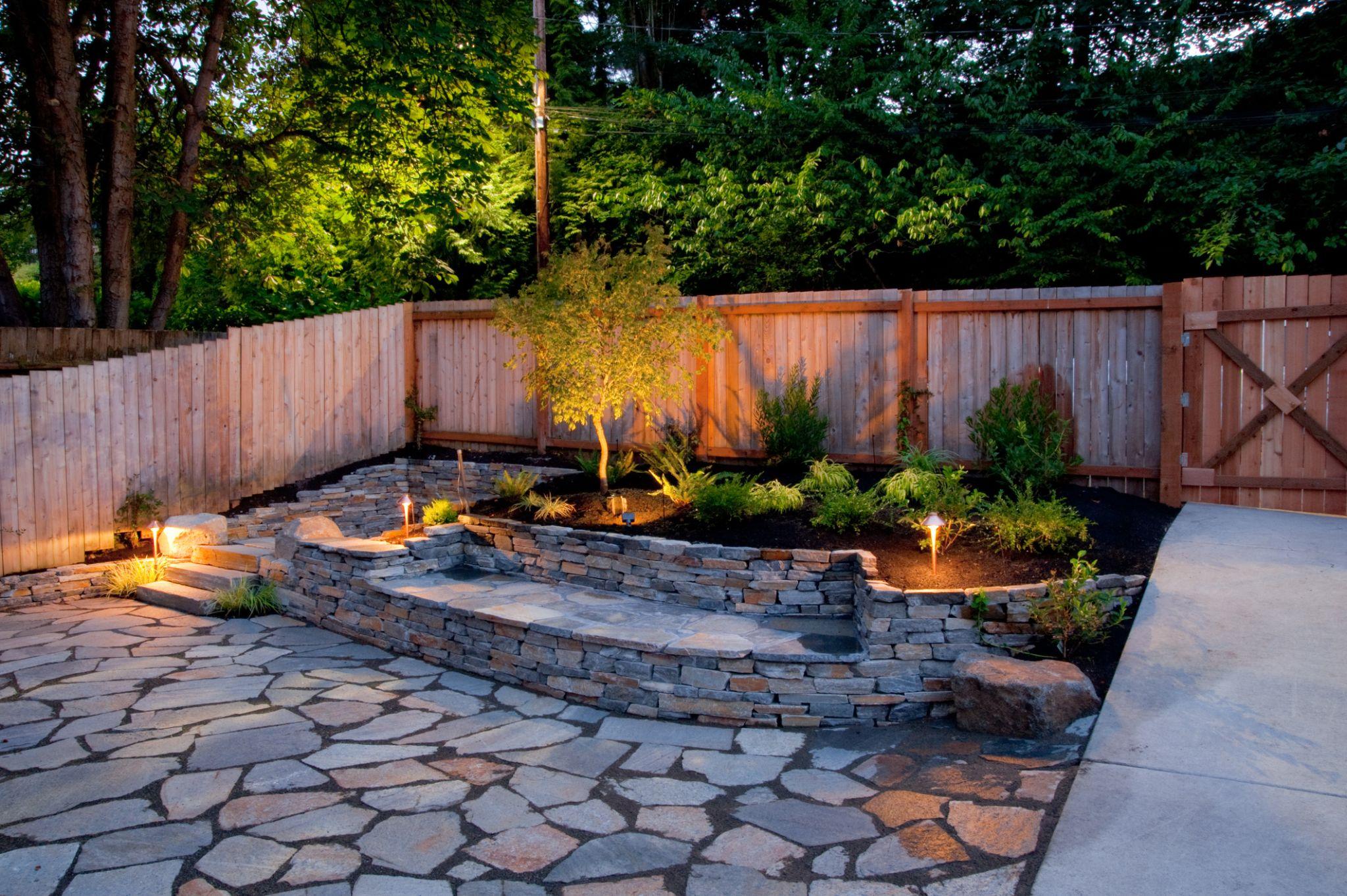 Backyard patio with stone retaining wall and landscape lighting at dusk
