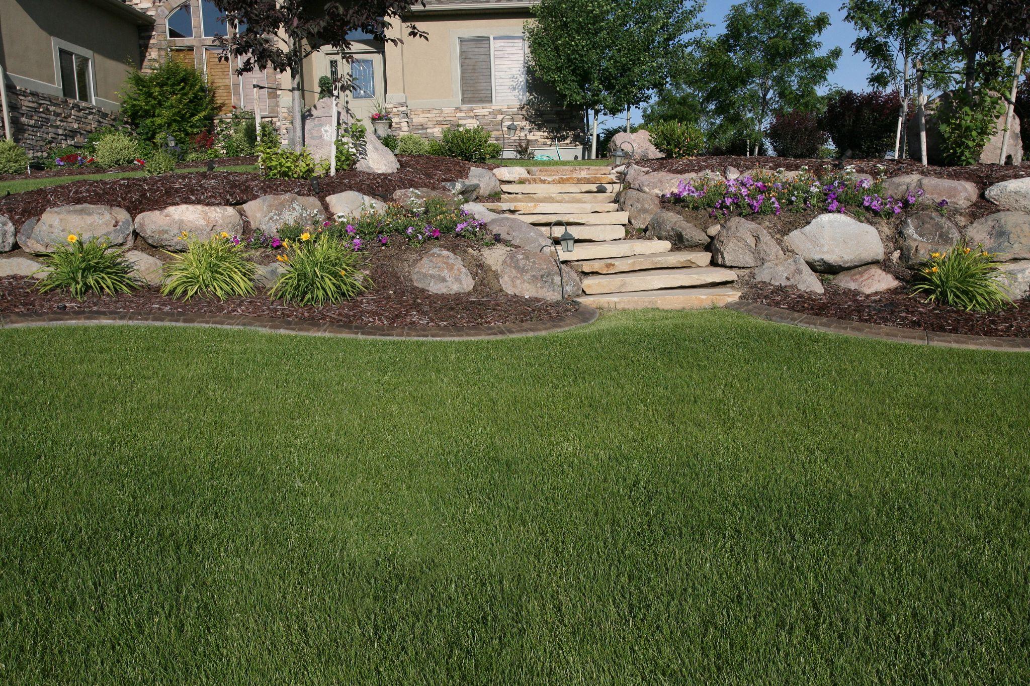 Boulder and stone retaining wall with flagstone steps, flowers, and manicured lawn