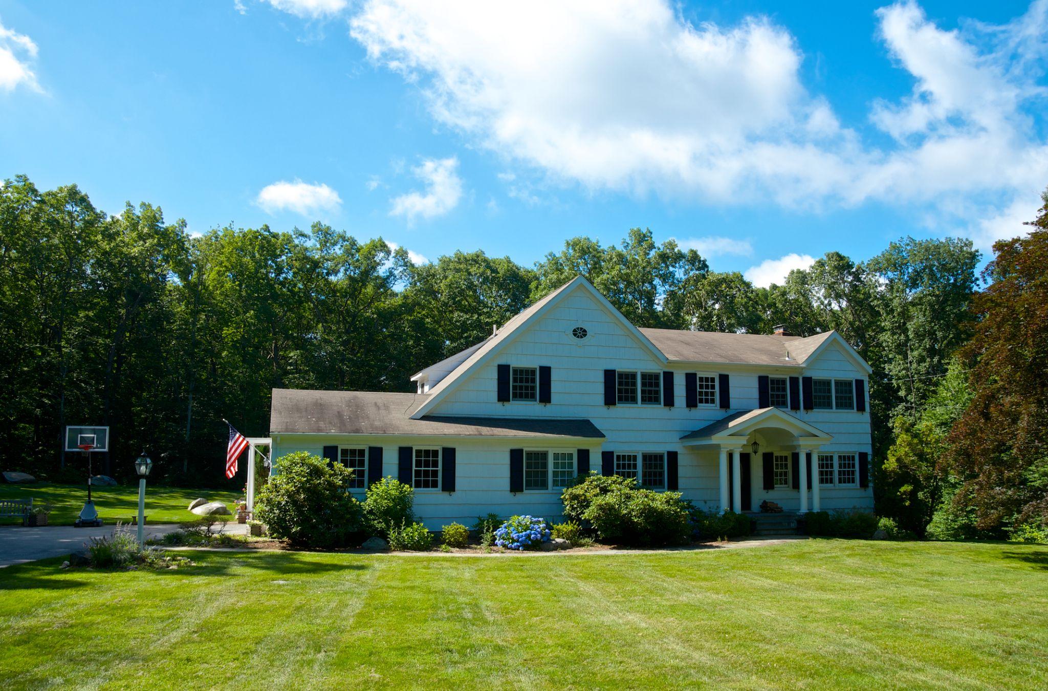 Colonial home with manicured green lawn and mature trees