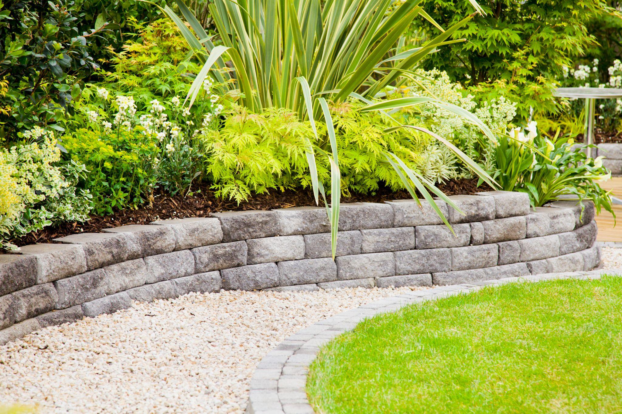 Curved concrete block retaining wall with lush garden planting and gravel border