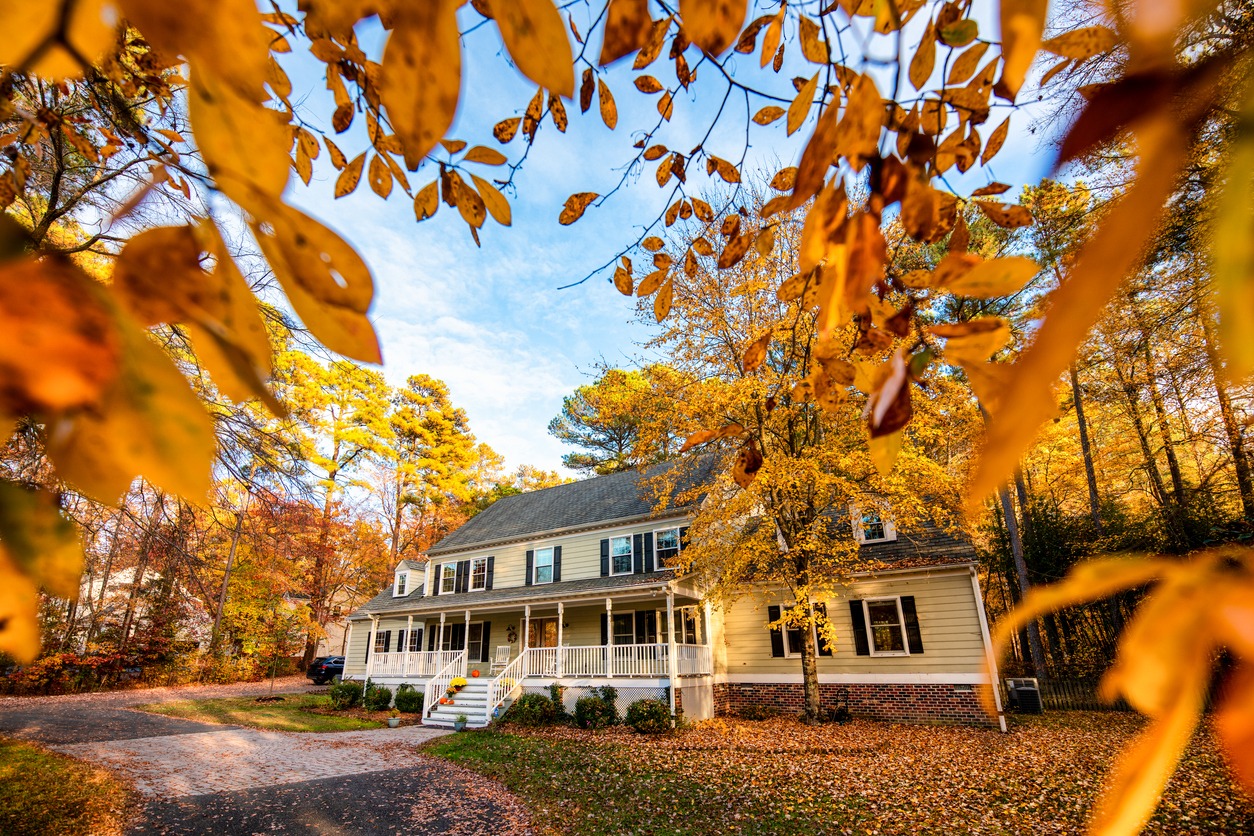 Home with colorful fall trees and leaves on the ground.