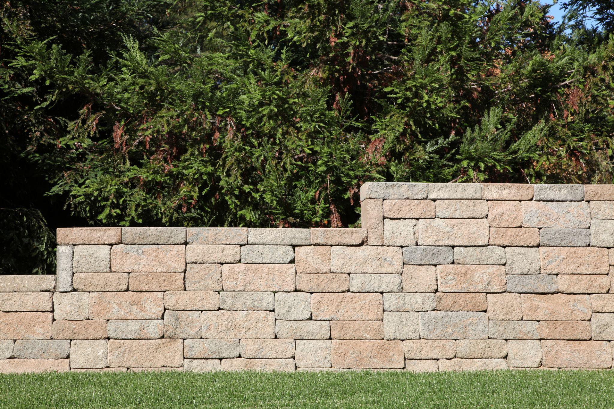 Segmental concrete block retaining wall with evergreen trees in background