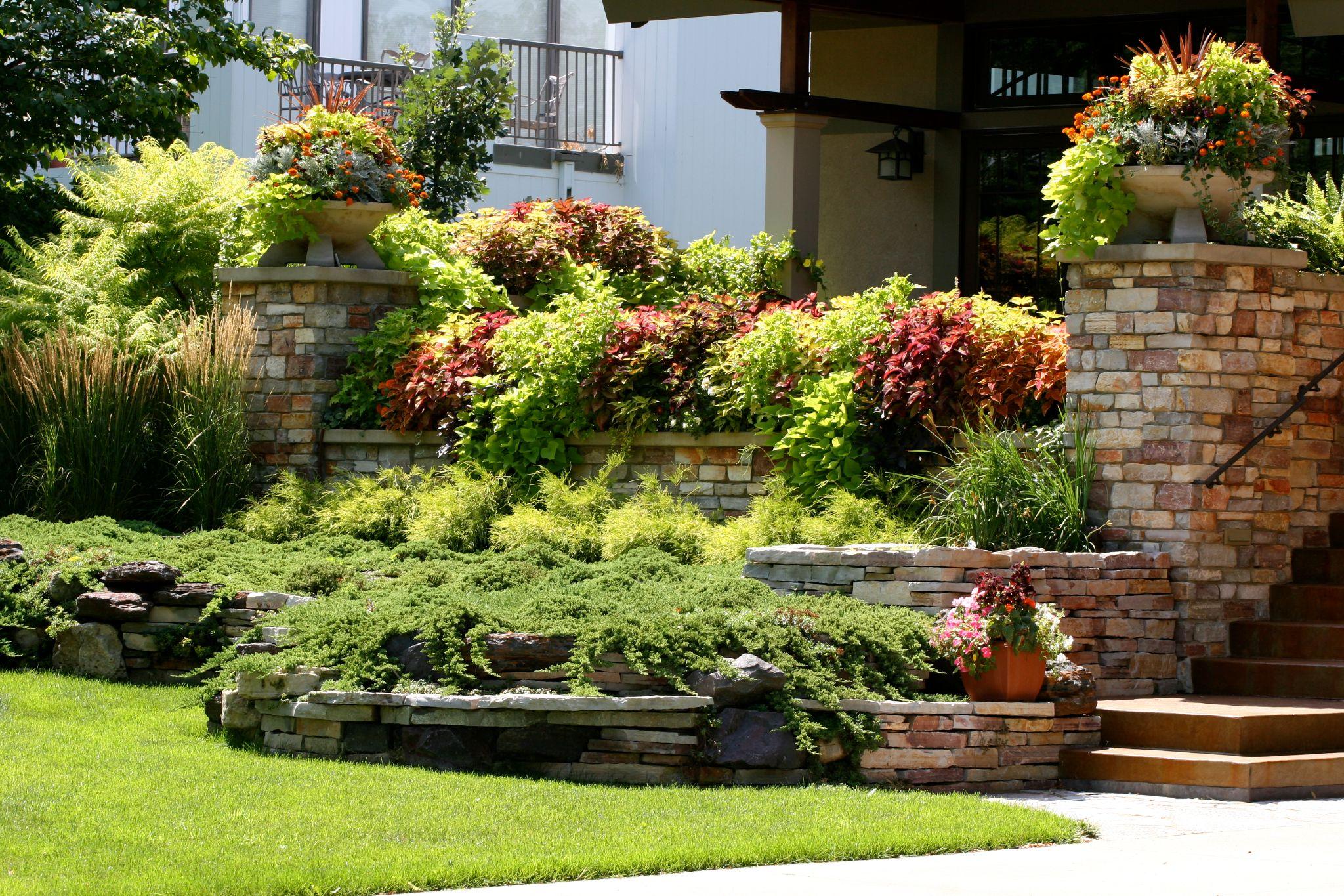 Tiered stone retaining walls with colorful plantings and decorative urns at home entrance