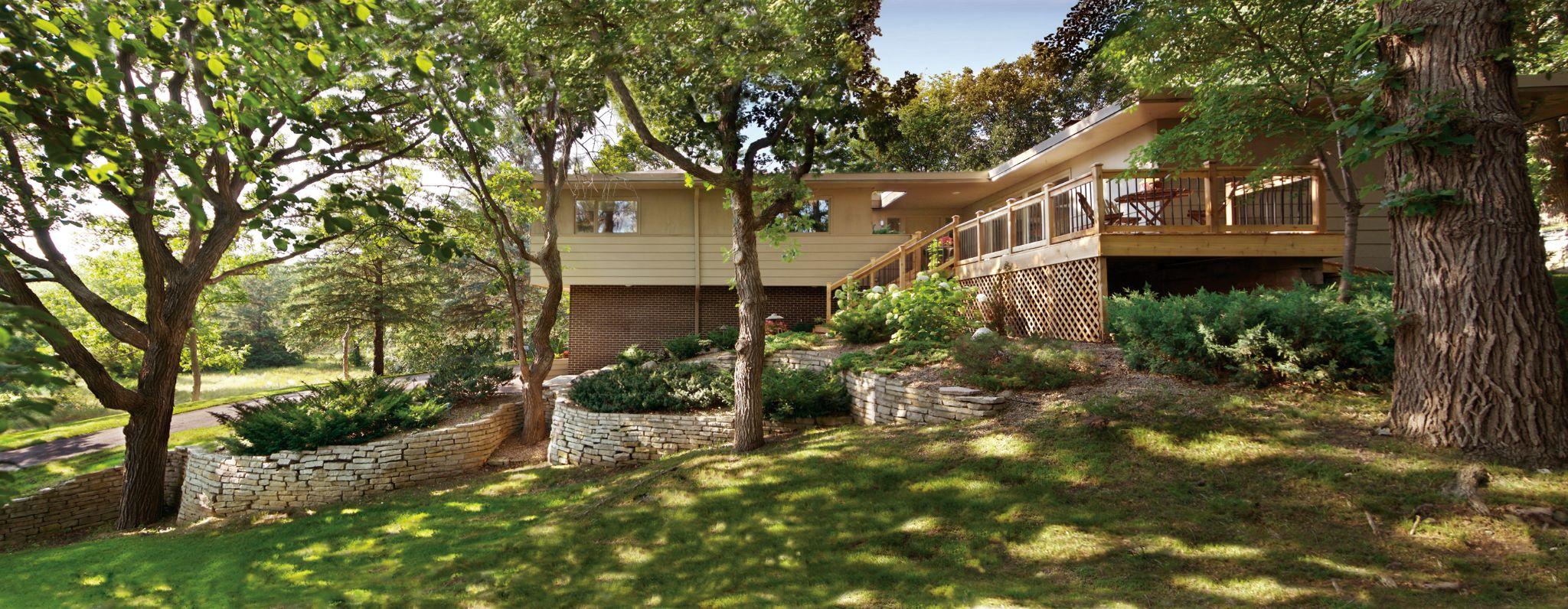 Wooded home exterior with tiered stone retaining walls and elevated wood deck